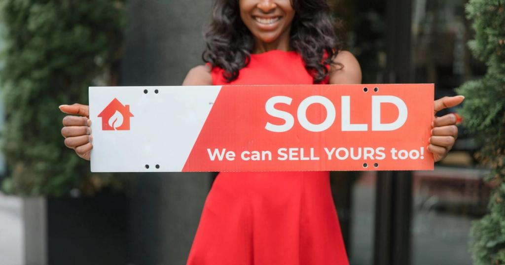 Smiling woman holding a 'Sold' sign, symbolizing successful real estate sales.