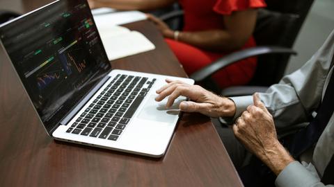 Business professionals analyzing stock market data on a laptop during a meeting.