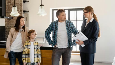 Family with child talks to real estate agent in modern kitchen during home showing.
