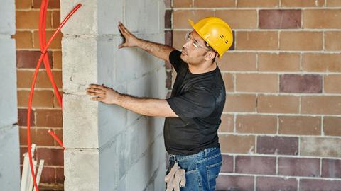Man in hard hat checks brick wall in indoor construction site.
