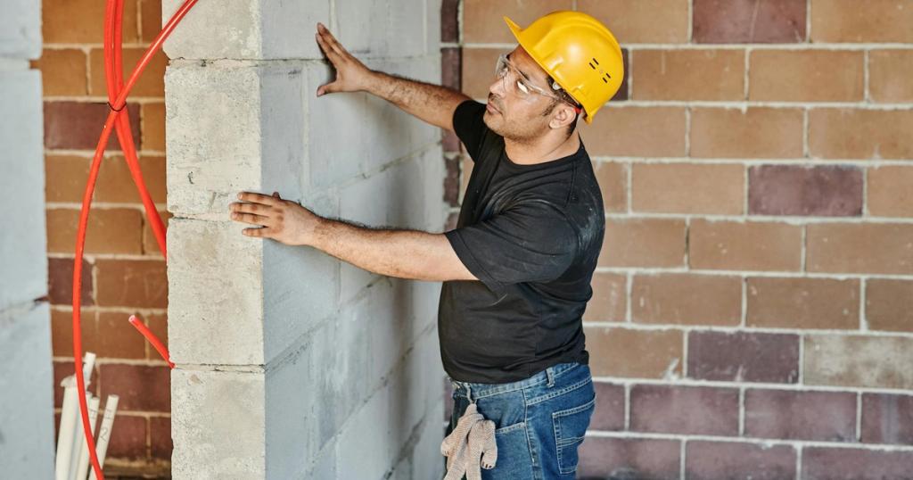Man in hard hat checks brick wall in indoor construction site.