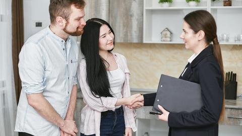 A young couple shakes hands with a real estate agent during a home tour or negotiation in a modern setting.