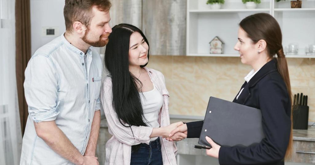 A young couple shakes hands with a real estate agent during a home tour or negotiation in a modern setting.