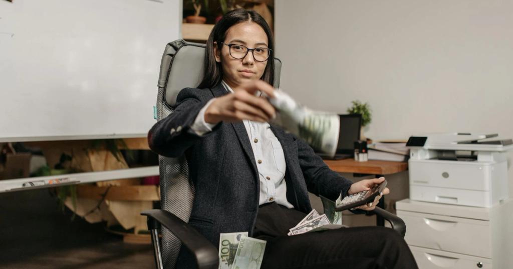 Confident businesswoman in eyeglasses counting dollar bills while sitting in a modern office.