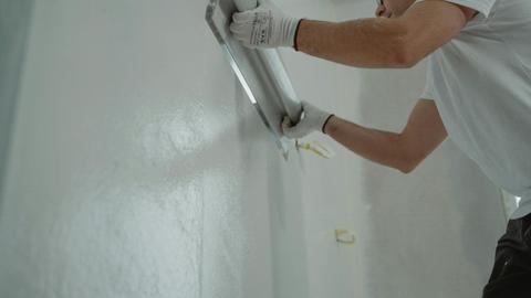 A man works on home renovation, applying plaster to an interior wall for a smooth finish.