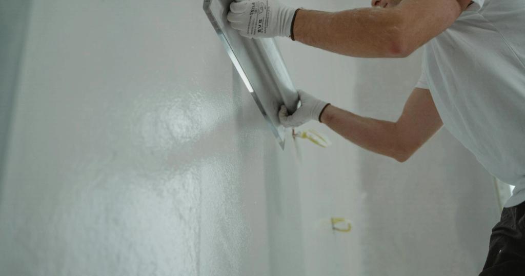 A man works on home renovation, applying plaster to an interior wall for a smooth finish.
