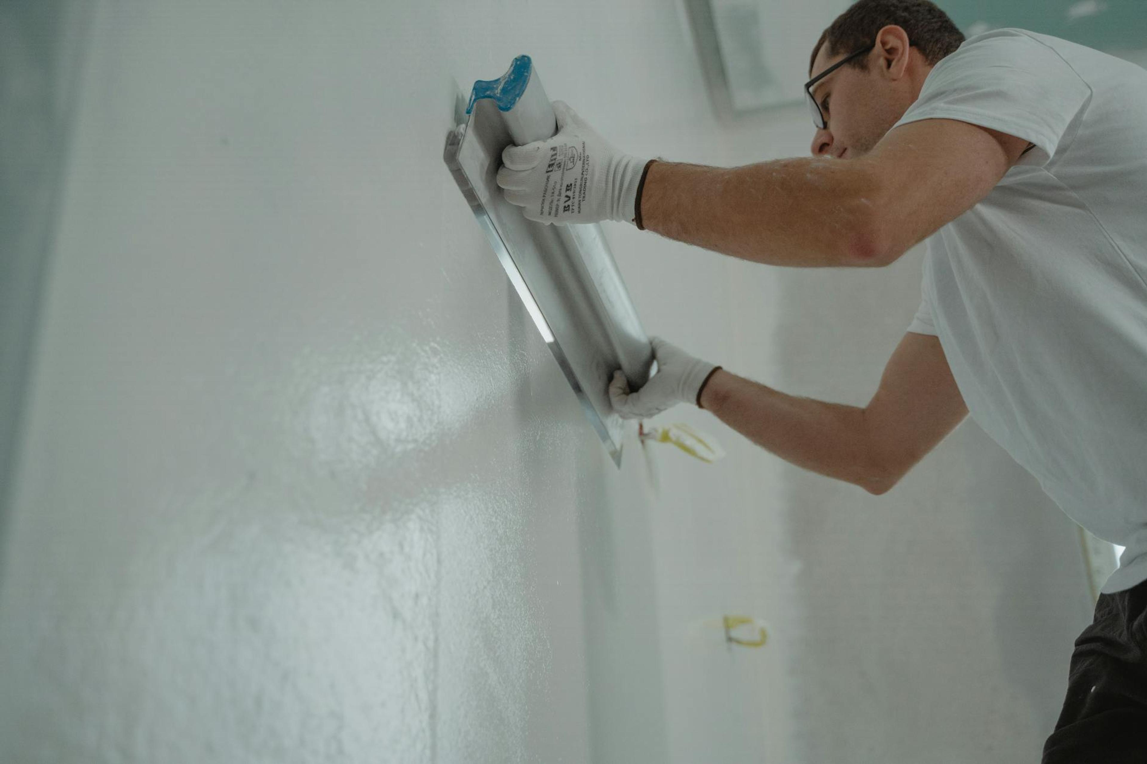 A man works on home renovation, applying plaster to an interior wall for a smooth finish.