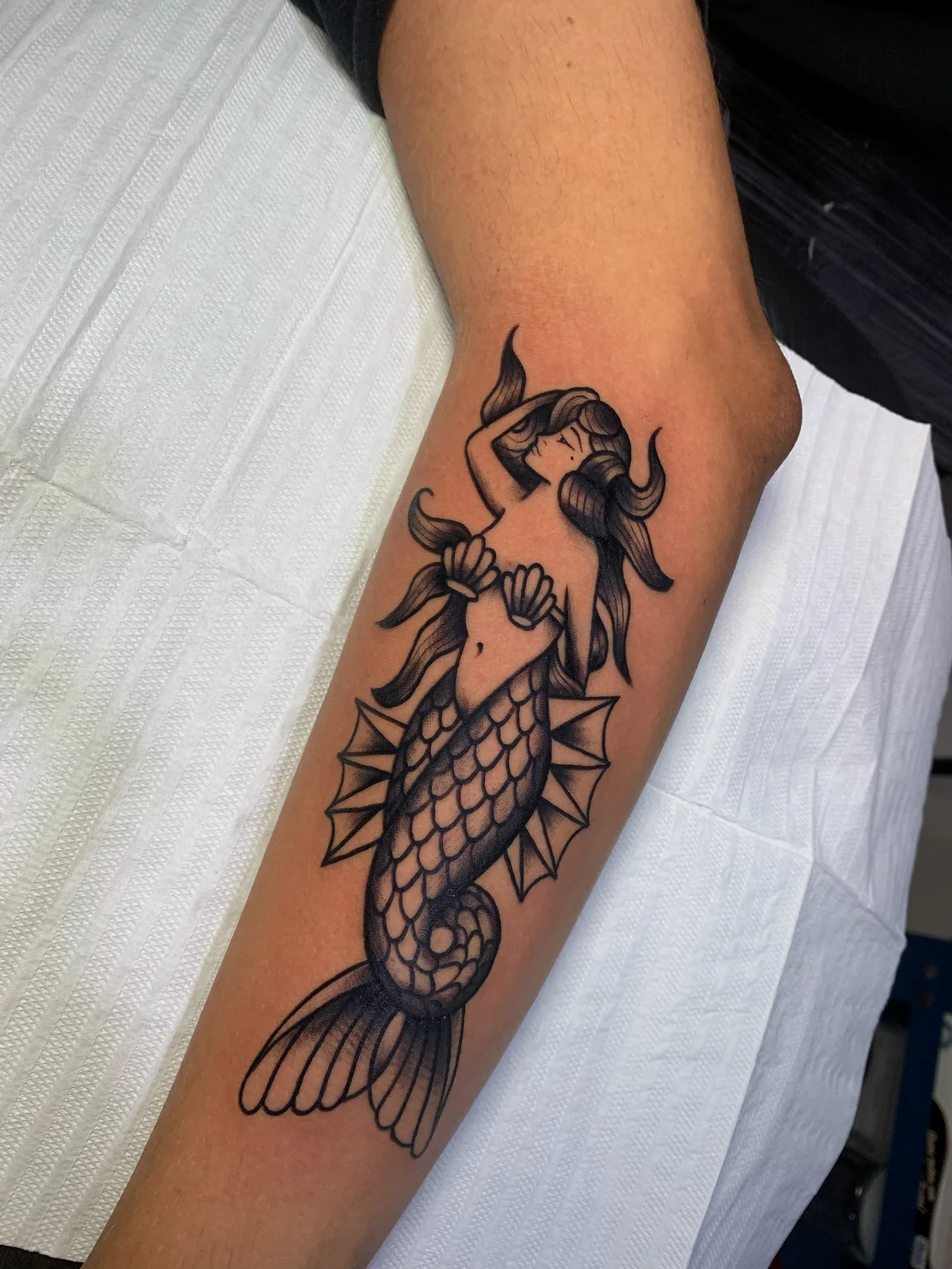 Tatuagem de sereia em traço preto no antebraço