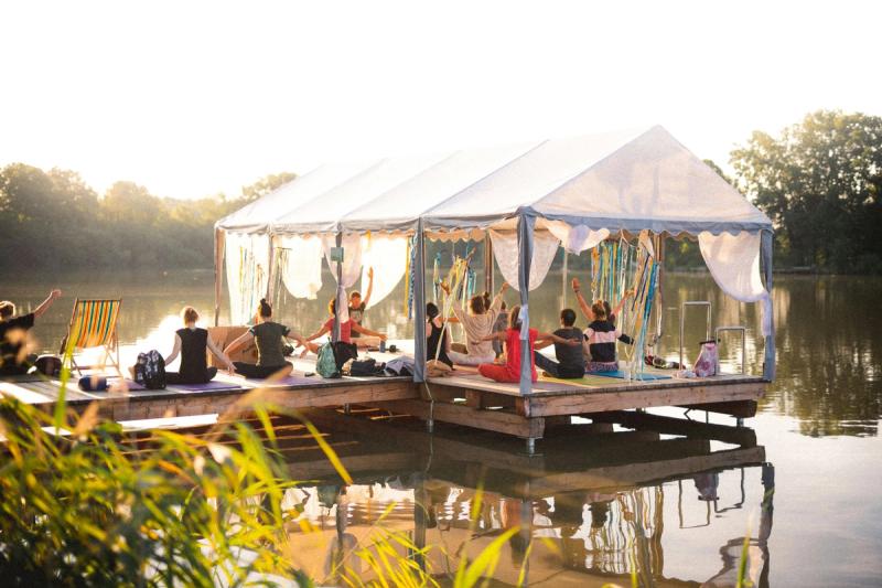 a group of people practice yoga on a dock under a tent with streamers