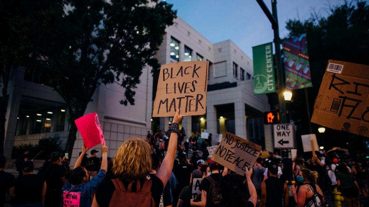 Image depicting a group of people with their body away from the camera point-of-view with placards reading 'Black Lives Matter'.