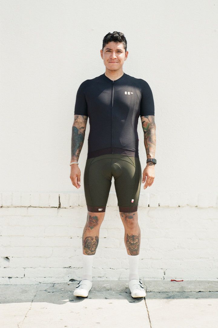 portrait of brian in front of a white wall, wearing everyone jersey in black and olive dance bibs