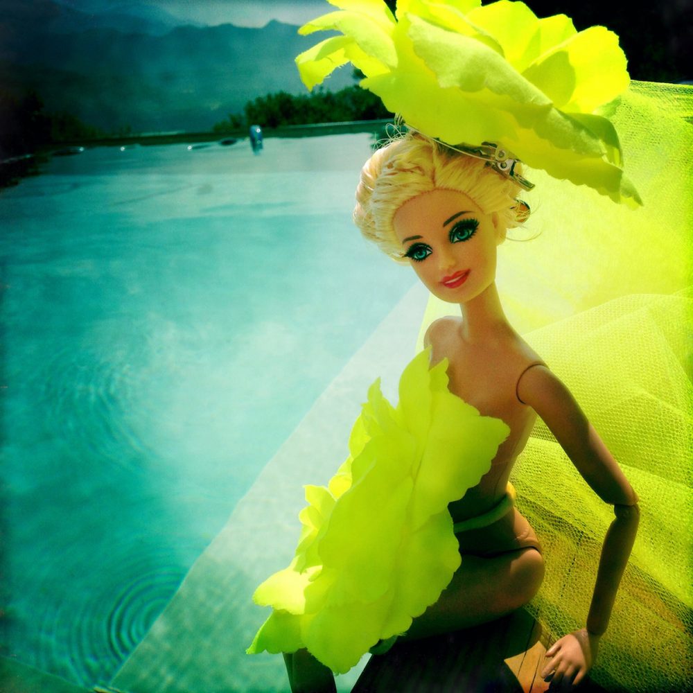 Barbie Delia Dickmann in piscina vestita con un abito giallo neon e una rosa gigante in testa