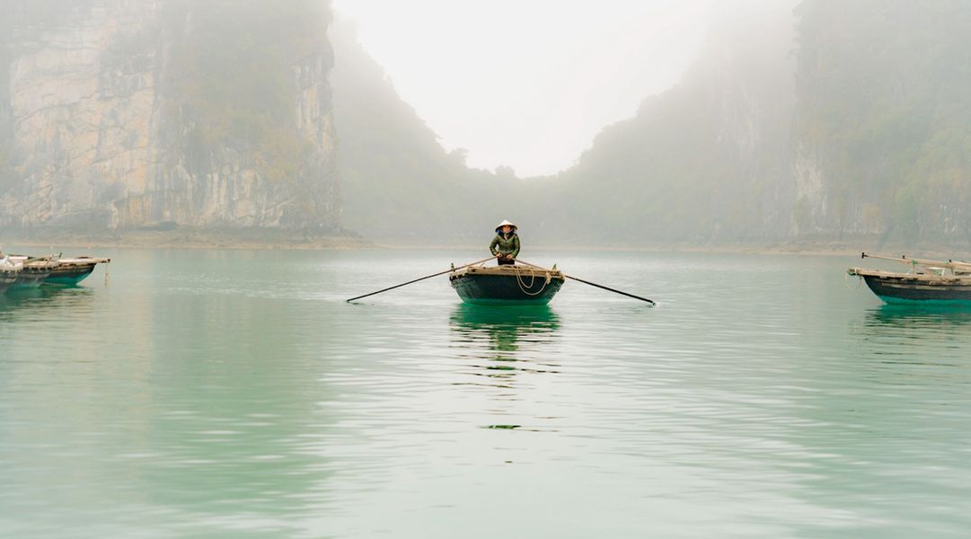 Georgia Ortner Fotografie vietnamesischer Boot Fahrer mit Hut auf türkisem Wasser in einem Tal