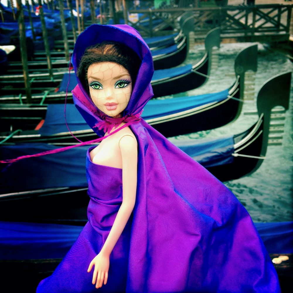 Delia Dickmann Fotografie brünette Barbie mit lila Cape und Kleid vor Holzboten in Venedig