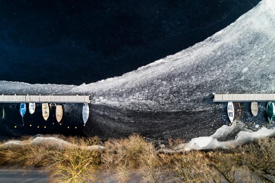 Stefan Kuhn's "Frozen Boats #03" Drohnenfotografie zeigt ein Seeufer mit Boot anlege Steg.