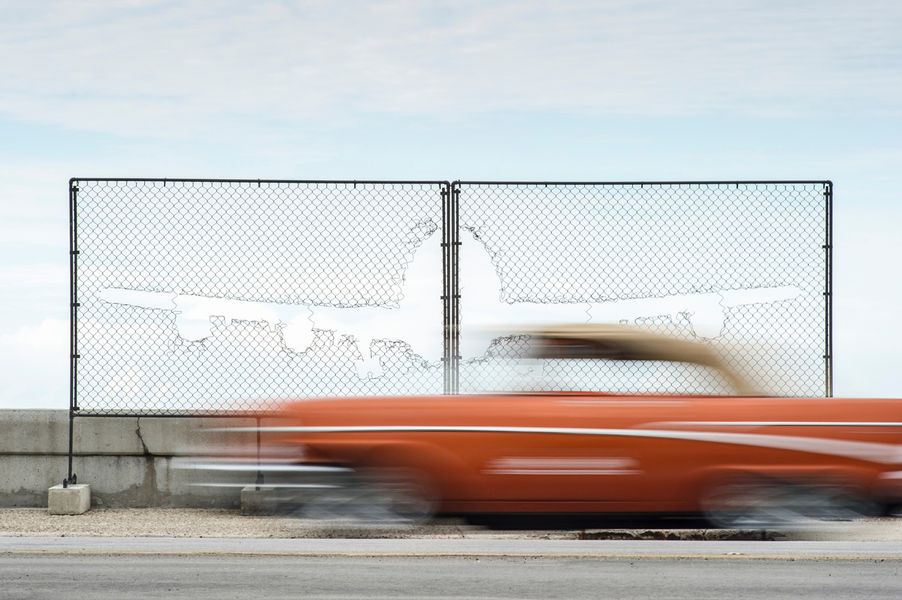 Joe Willems photography vintage car in motion blur with fence and hole in the shape of a plane in the background and blue sky