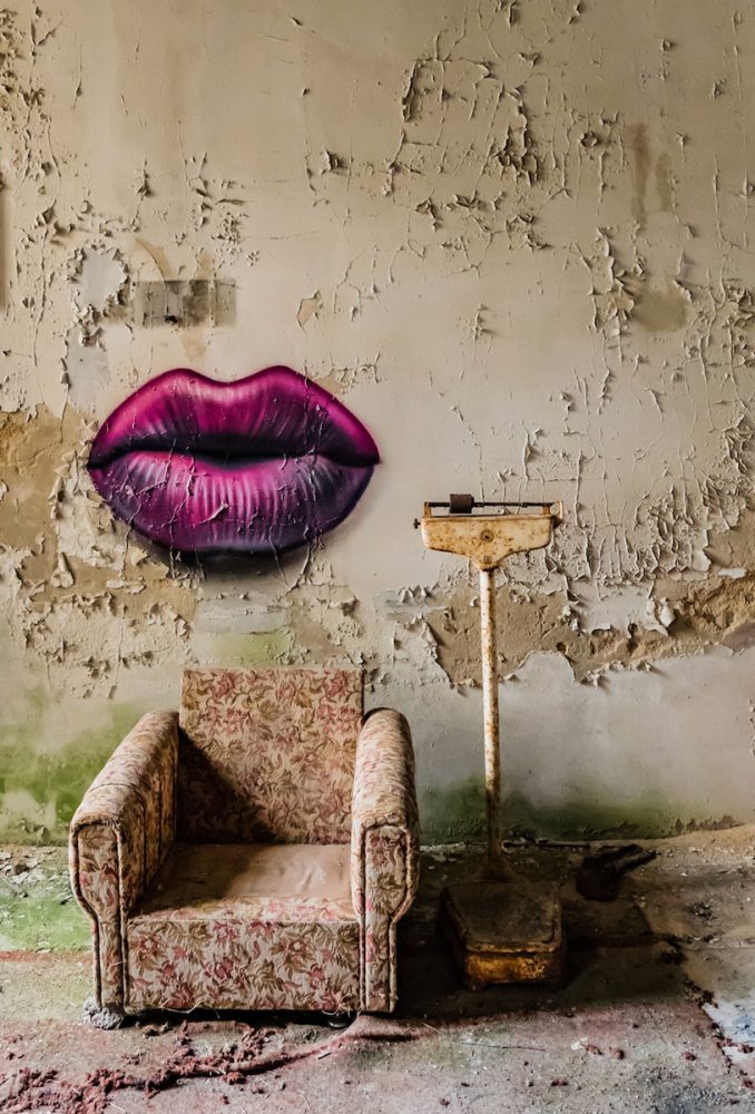Georgia Ortner Photographie lost place Canapé unique et vieille balance devant un mur friable avec une bouche à baiser violette