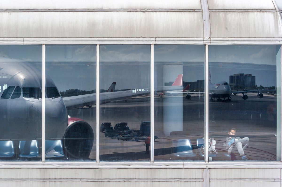 Joe Willems Airport terminal window front sitting man and large reflection of an aeroplane