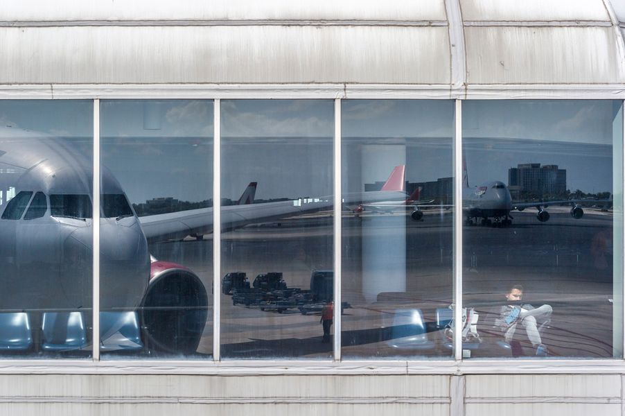 Joe Willems Airport terminal window front sitting man and large reflection of an aeroplane