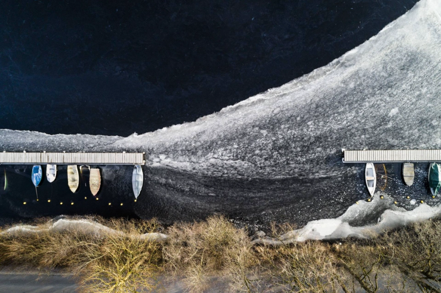 Stefan Kuhn's "Frozen Boats #03" Drohnenfotografie zeigt ein Seeufer mit Boot anlege Steg.