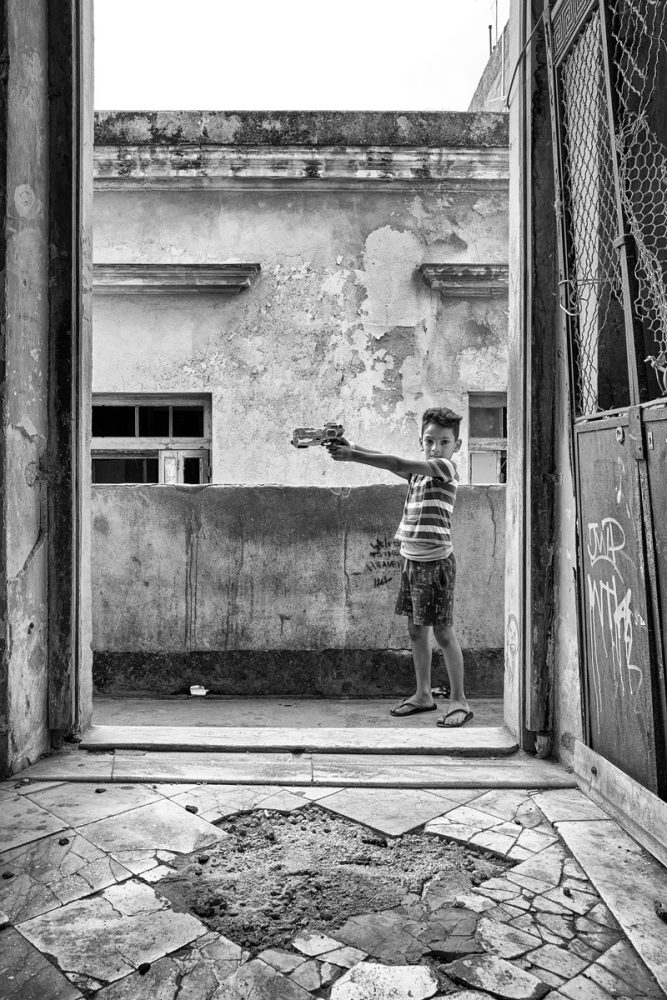Joe Willems Fotografie schwarzweiß Kind mit Plastik Pistole auf altem Stein Balkon