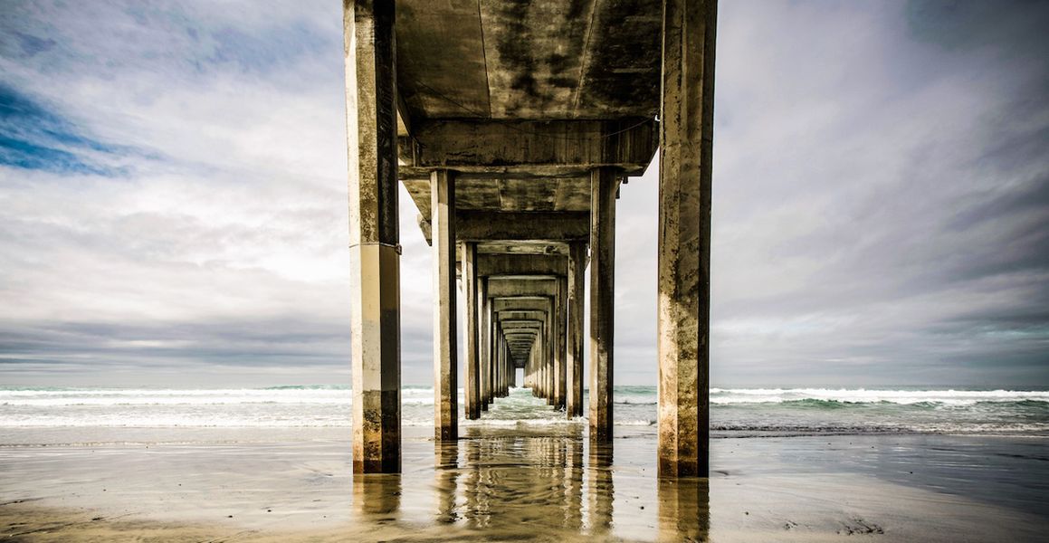Georgia Ortner Photography Underside of a jetty on the beach in the water with blue sky
