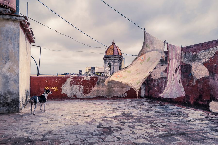 Joe Willems photography old crumbling terrace in Cuba with two sheets on clothesline and dog with church in background