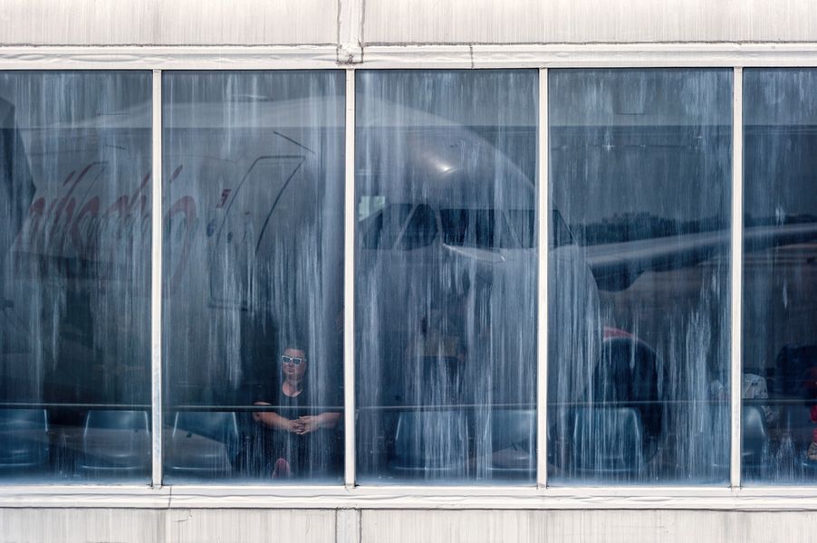 Joe Willems Fotografie Flughafen Terminal Fensterfront mit Frau in Sonnenbrille und große Spiegelung eines Flugzeuges