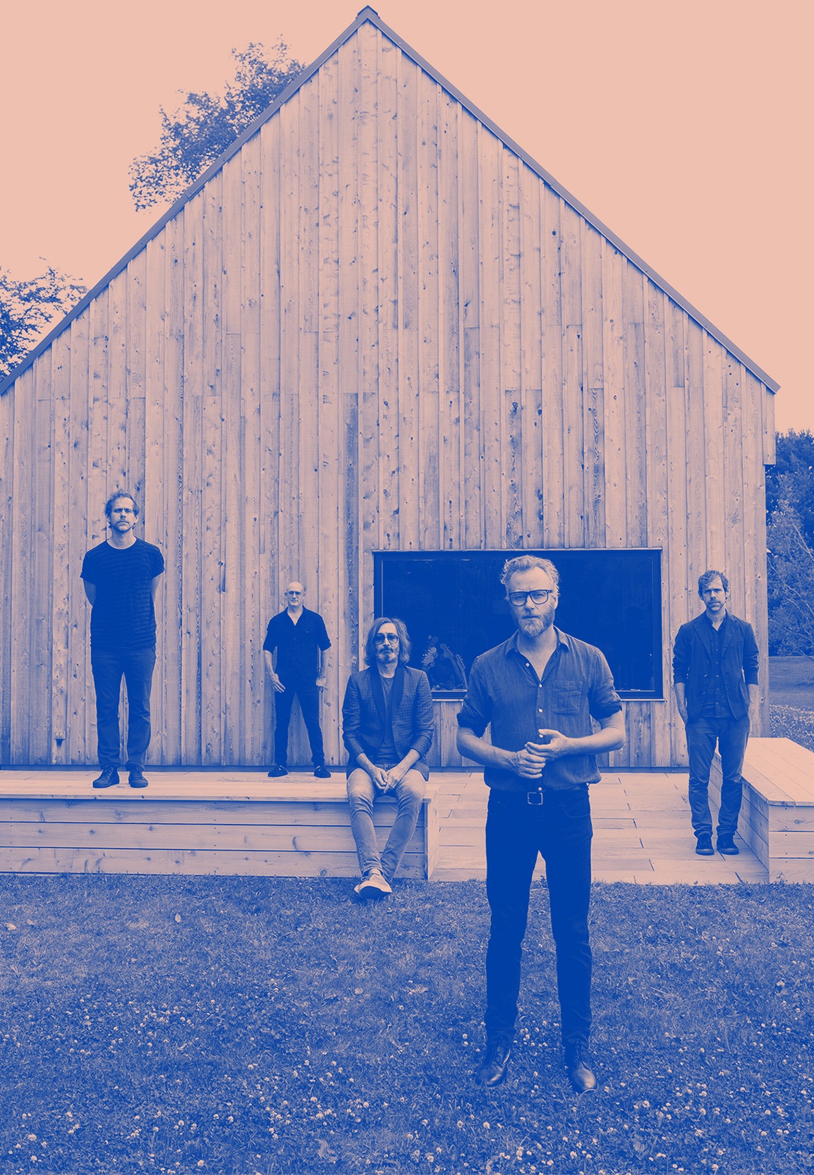 Blue and pink colorized photo of the band in front of Aaron Dessner's recording studio, a former barn dating back to the 18th century. All of the band members are standing or sitting at various distances from the camera.