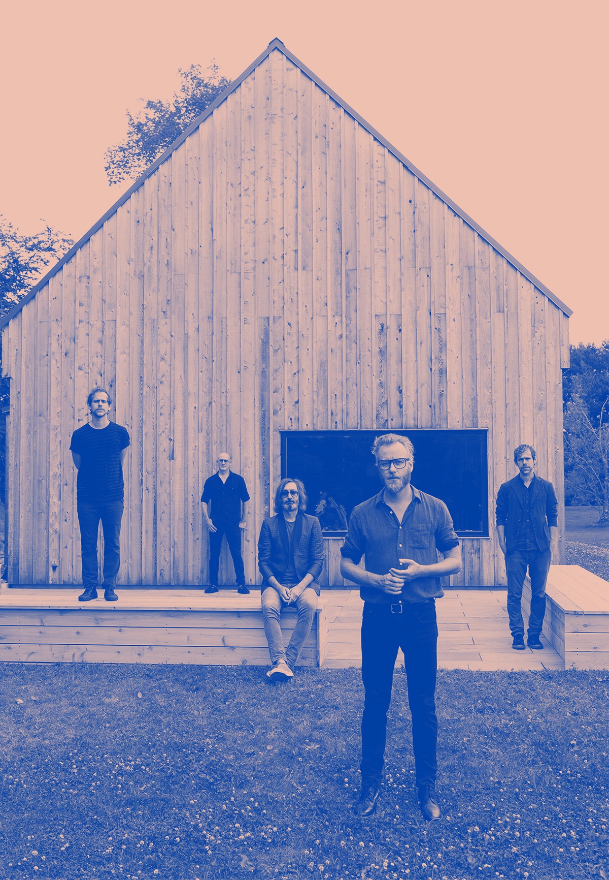Blue and pink colorized photo of the band in front of Aaron Dessner's recording studio, a former barn dating back to the 18th century. All of the band members are standing or sitting at various distances from the camera.