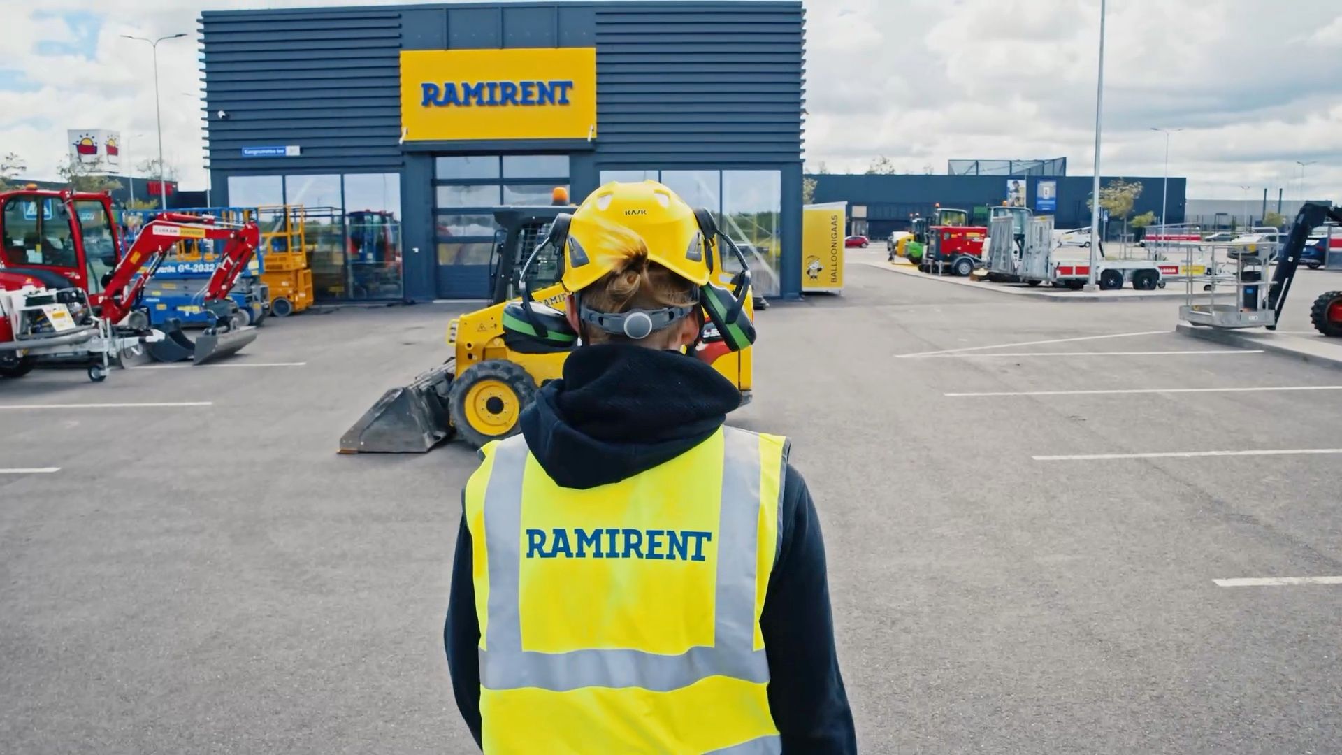 Worker in a Ramirent safety vest in front of the Ramirent depot, with a loader beside him