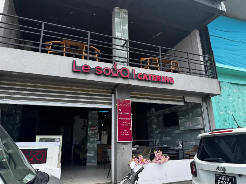 Le Souq Catering sign and a red opening-hours banner below an upper balcony, with a white Jeep parked outside