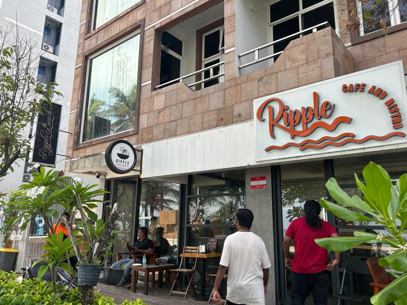 Ripple Cafe and Bistro corner storefront with orange wave logo sign and people walking past outdoor seating