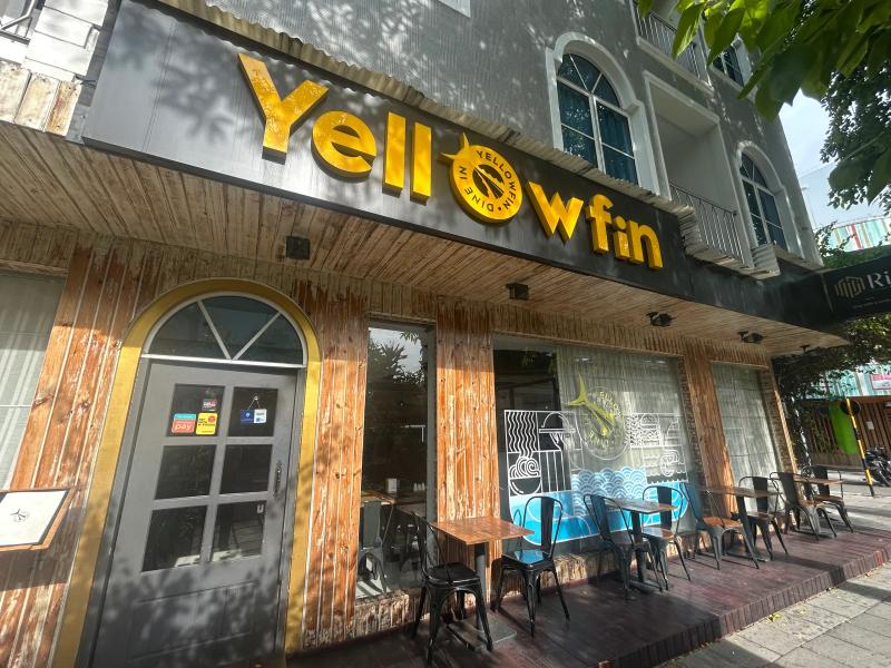 Yellowfin Dine-in storefront with bold yellow sign, wood-clad facade and metal chairs at pavement tables