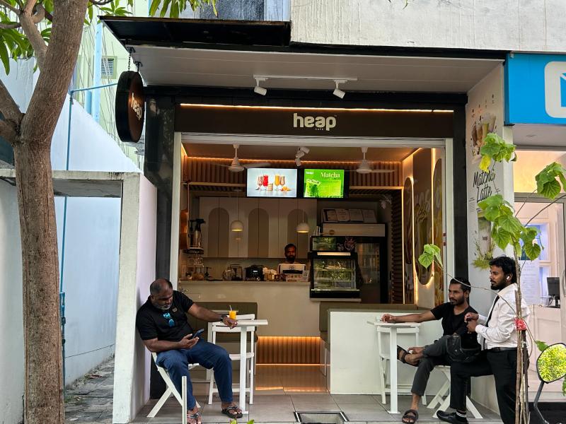 Open counter of Heap Cafe with menu screens, with people seated at white stools out front