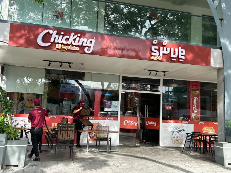 Chicking's red storefront with glass frontage, branded signs in English and Dhivehi, and staff setting up tables