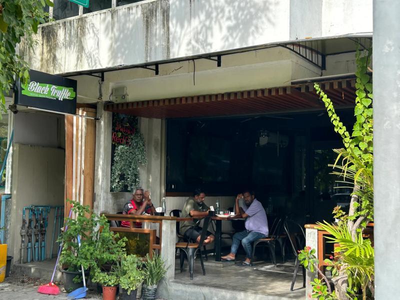 Black Truffle's green script sign on a corner cafe with an open-sided seating area and potted plants