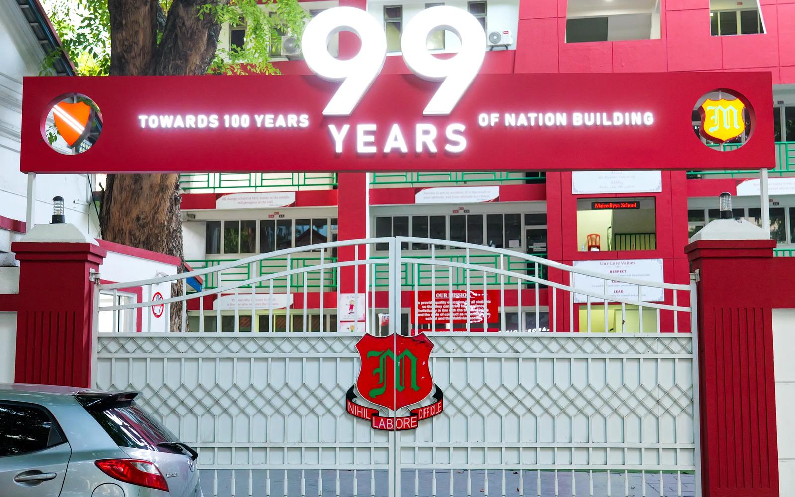 The red and white gate of Majeedhiyya School in Malé, with its 99 Years of Nation Building banner and the school crest