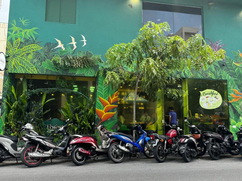 Tropical jungle mural on the green Foresta cafe facade with scooters parked along the street