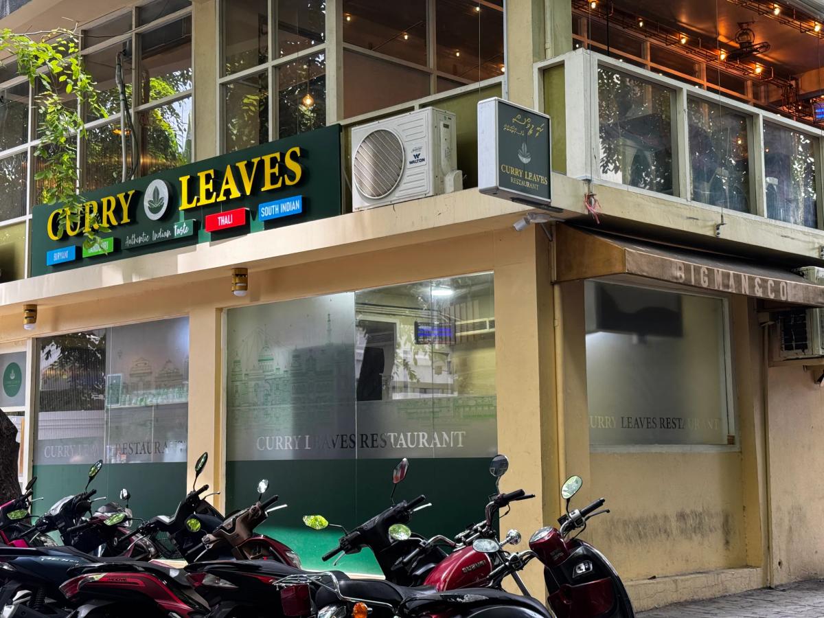 Curry Leaves' green and gold sign above frosted windows on a corner building, motorbikes parked outside