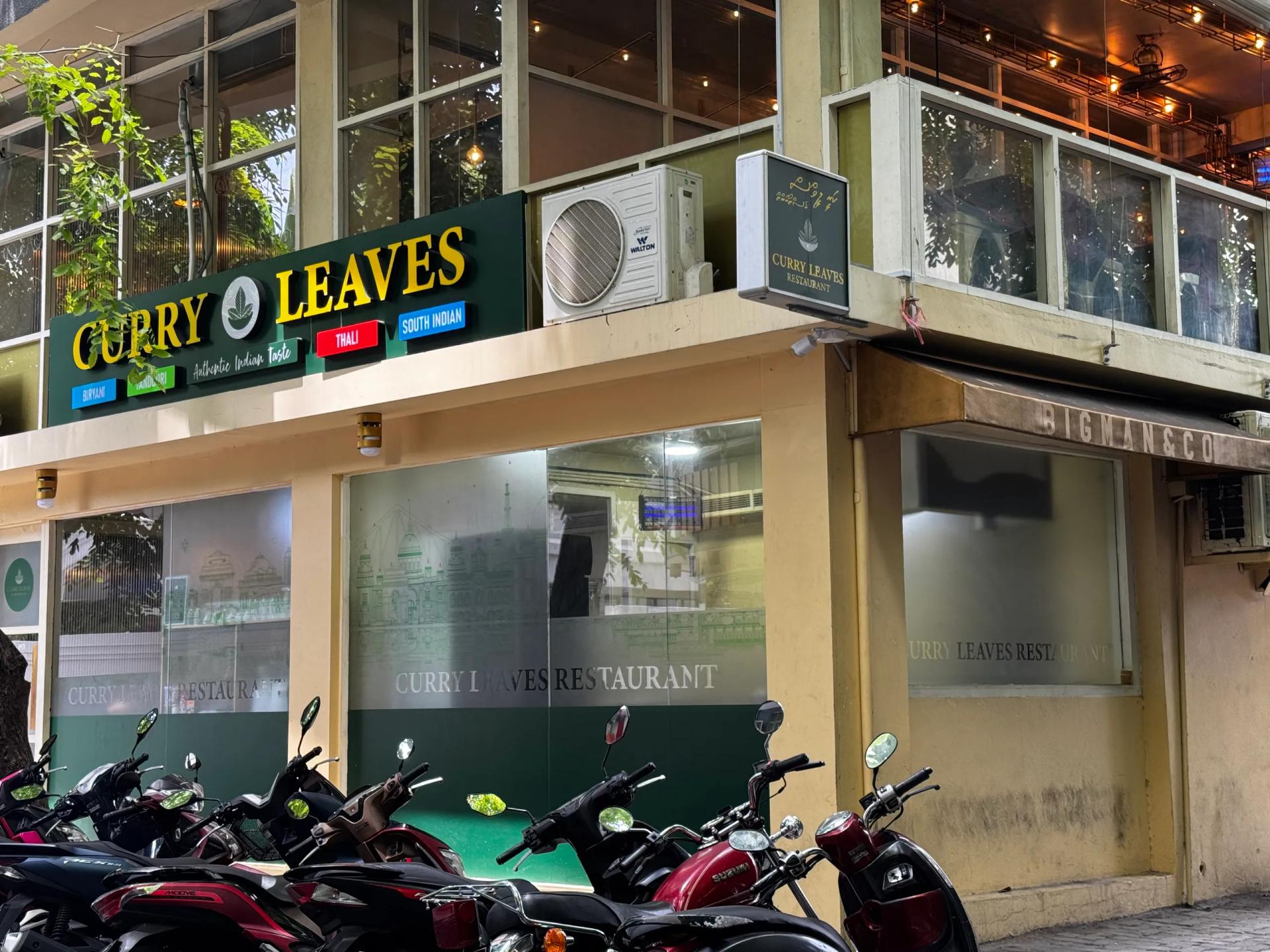 Curry Leaves' green and gold sign above frosted windows on a corner building, motorbikes parked outside