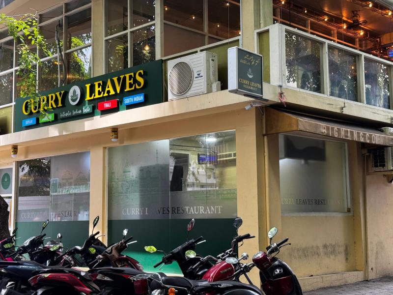 Curry Leaves' green and gold sign above frosted windows on a corner building, motorbikes parked outside