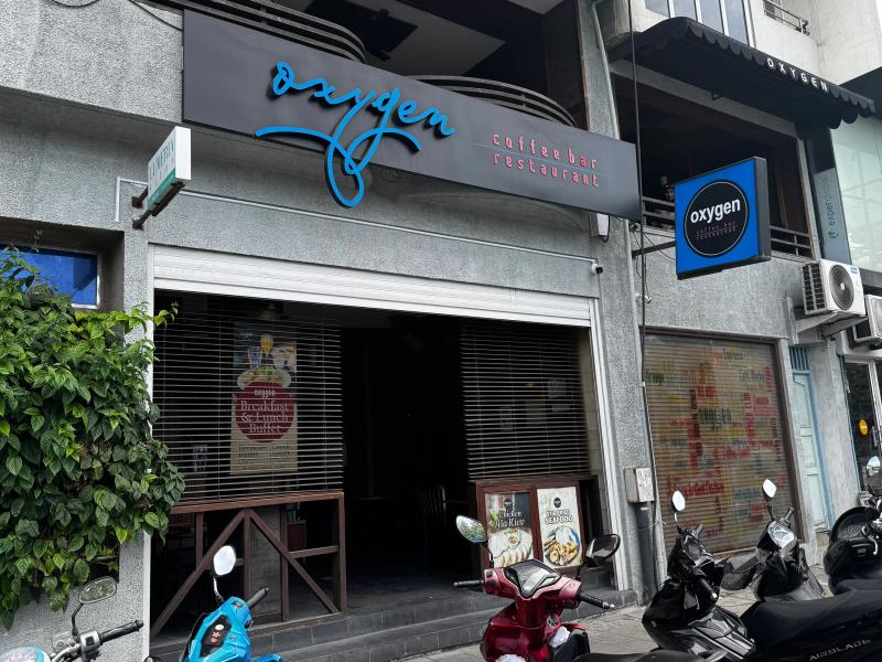 Grey street facade of Oxygen coffee bar and restaurant with blue script signage and parked motorbikes