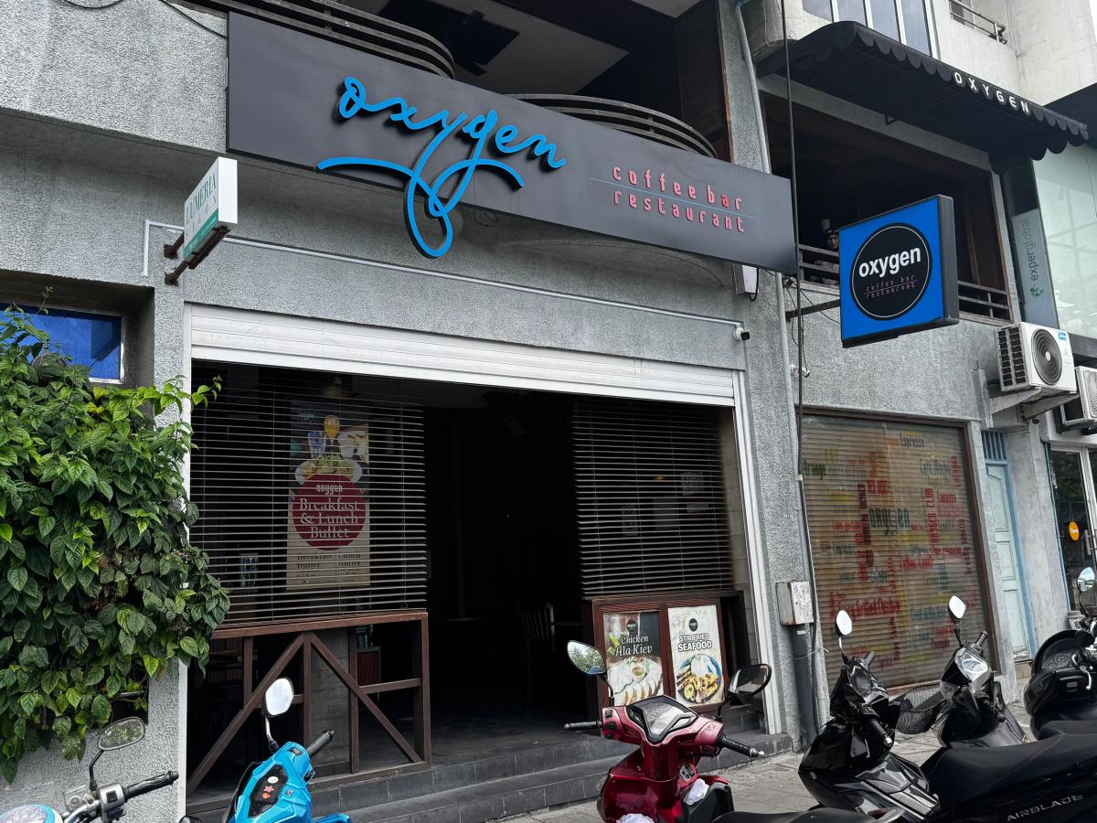 Grey street facade of Oxygen coffee bar and restaurant with blue script signage and parked motorbikes