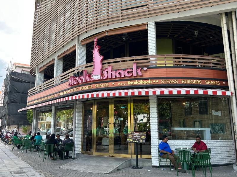 NY Steak Shack corner storefront with red-striped awning, Statue of Liberty logo and pavement seating