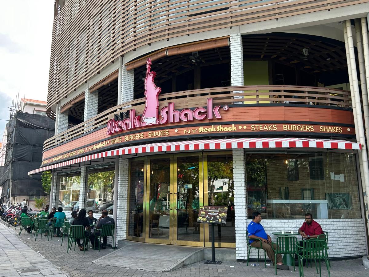 NY Steak Shack corner storefront with red-striped awning, Statue of Liberty logo and pavement seating