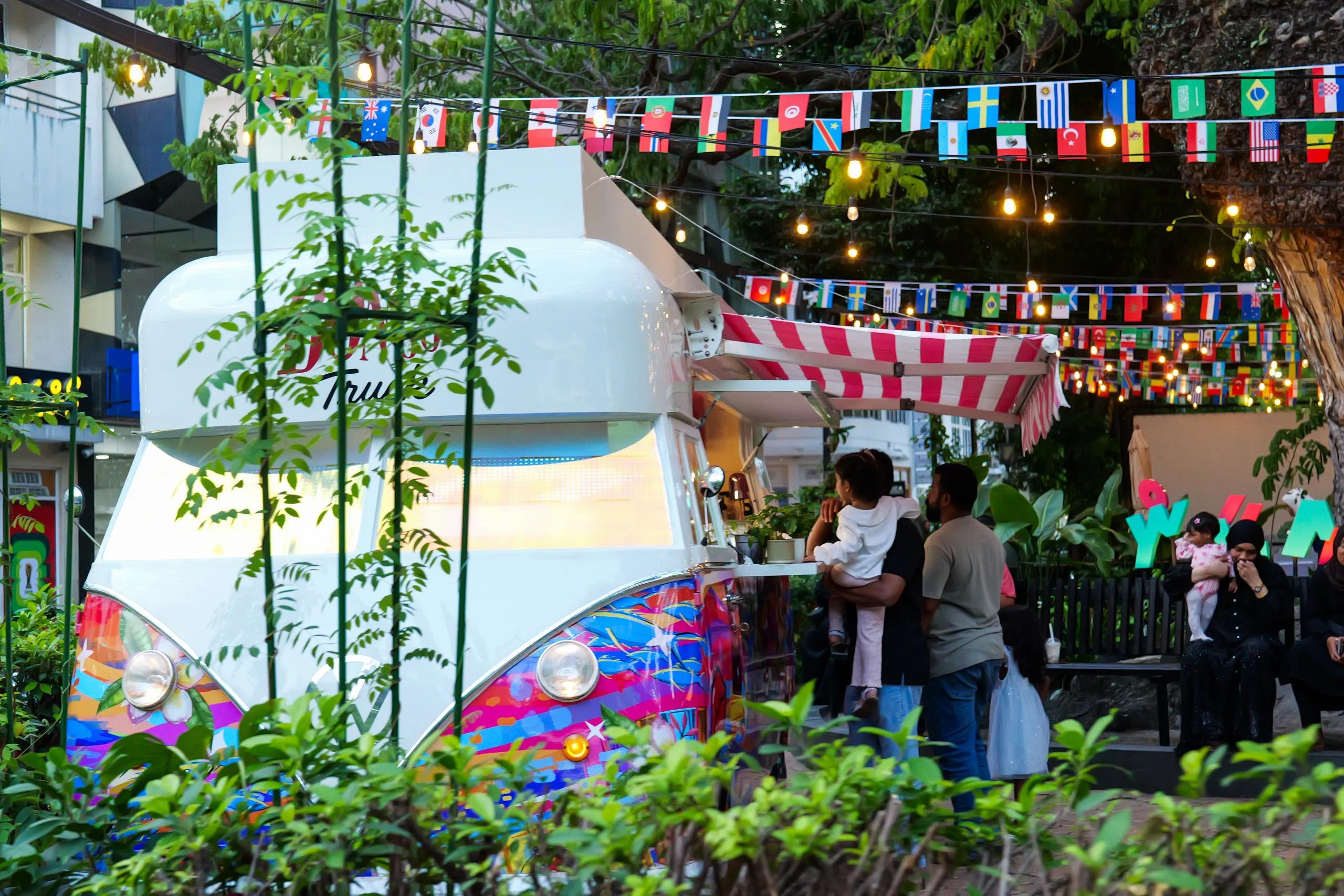 The Bongo Truck, a colourfully painted snack van with a striped awning, under string lights and flag bunting in Malé