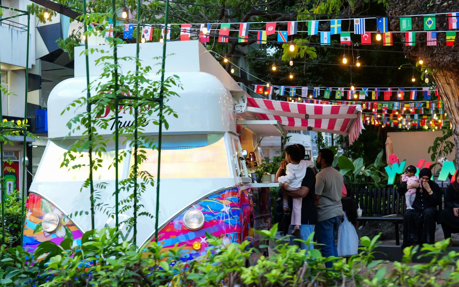The Bongo Truck, a colourfully painted snack van with a striped awning, under string lights and flag bunting in Malé