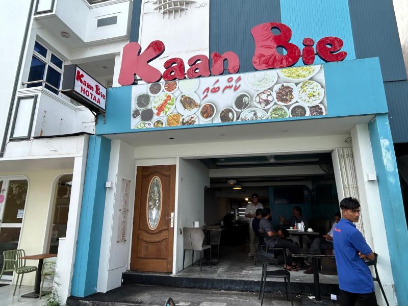 Kaan Bie Hotaa entrance with a food-photo banner overhead and diners seated inside the dim interior