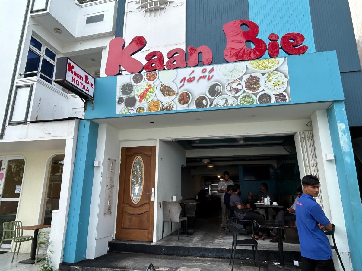 Kaan Bie Hotaa entrance with a food-photo banner overhead and diners seated inside the dim interior